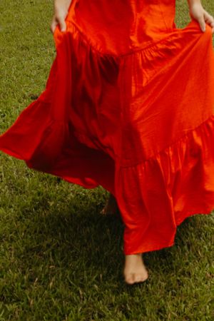 A person wearing a flowing red maxi dress twirls on green grass with bare feet visible under the ruffled hem.