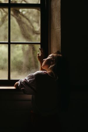 A silhouetted figure gazes out of a dark window with dramatic lighting and moody atmosphere.