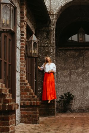 A person in vintage attire stands on brick steps near antique lanterns in an old stone building.