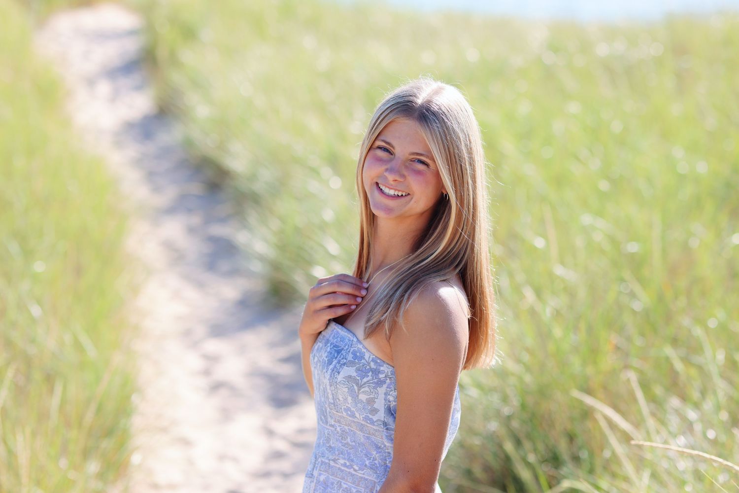 Portrait of woman in pink top smiling at beach during golden hour.