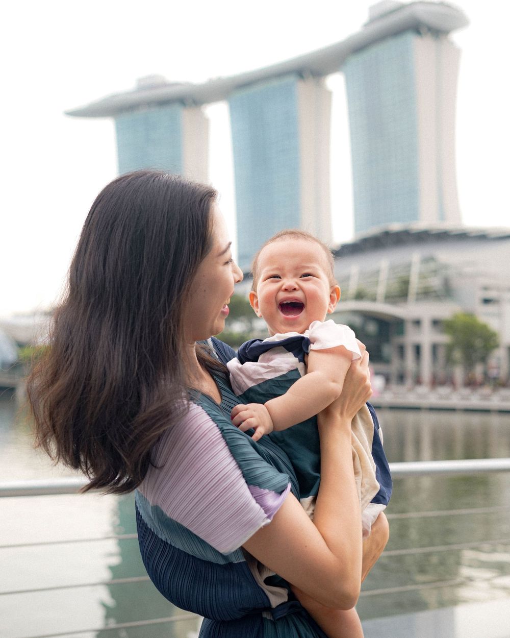 A mother holds her laughing baby with Marina Bay Sands in the background.