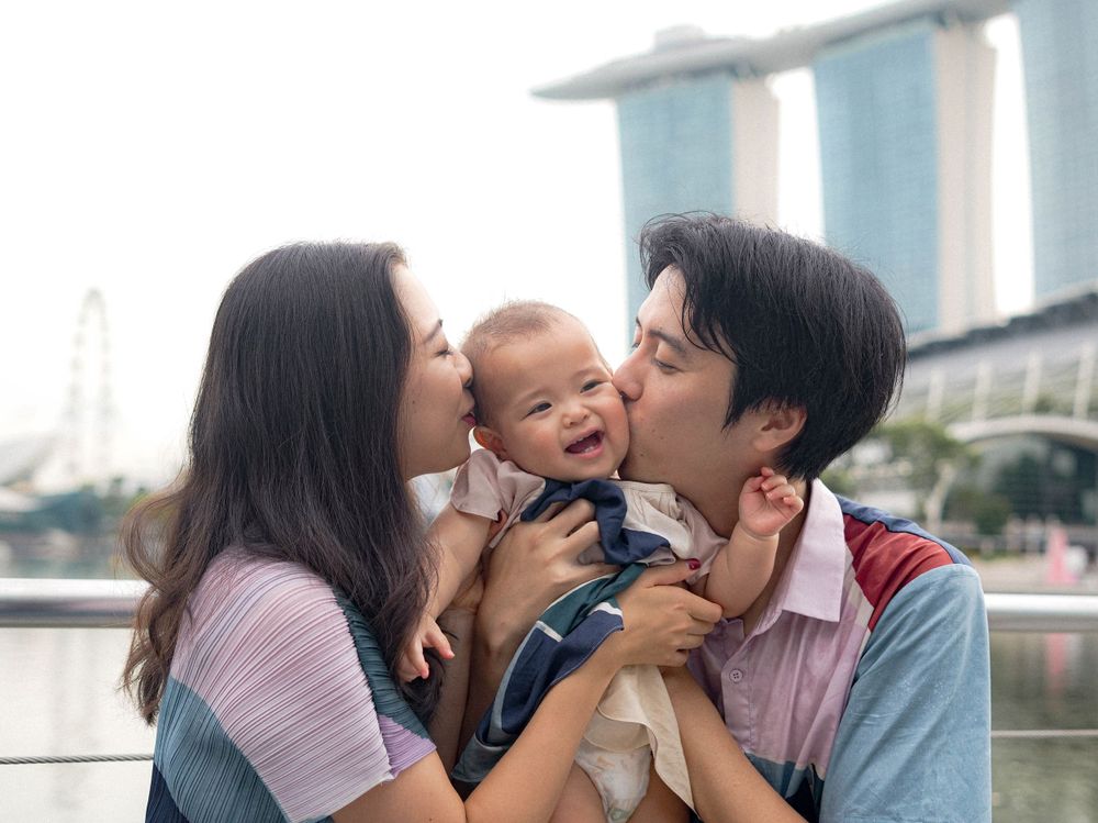 Parents shower their laughing baby with kisses at Singapore's waterfront.