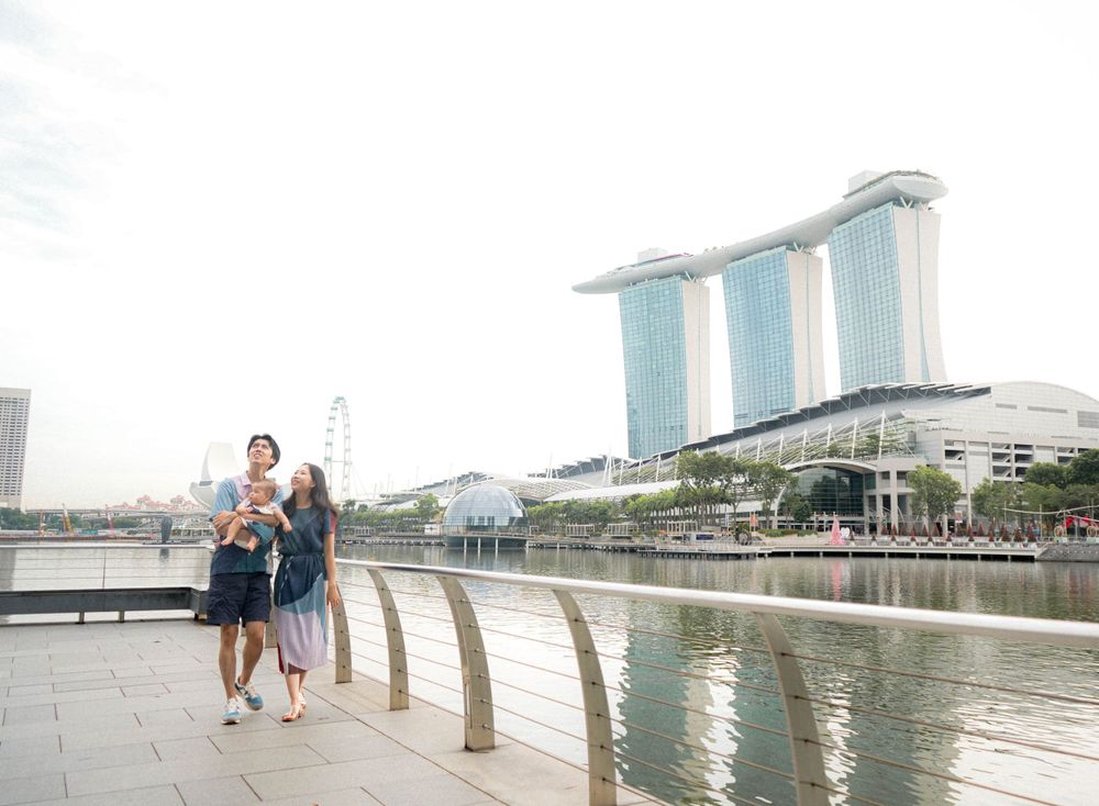 A family takes a stroll along Marina Bay waterfront with iconic hotel towers in background.