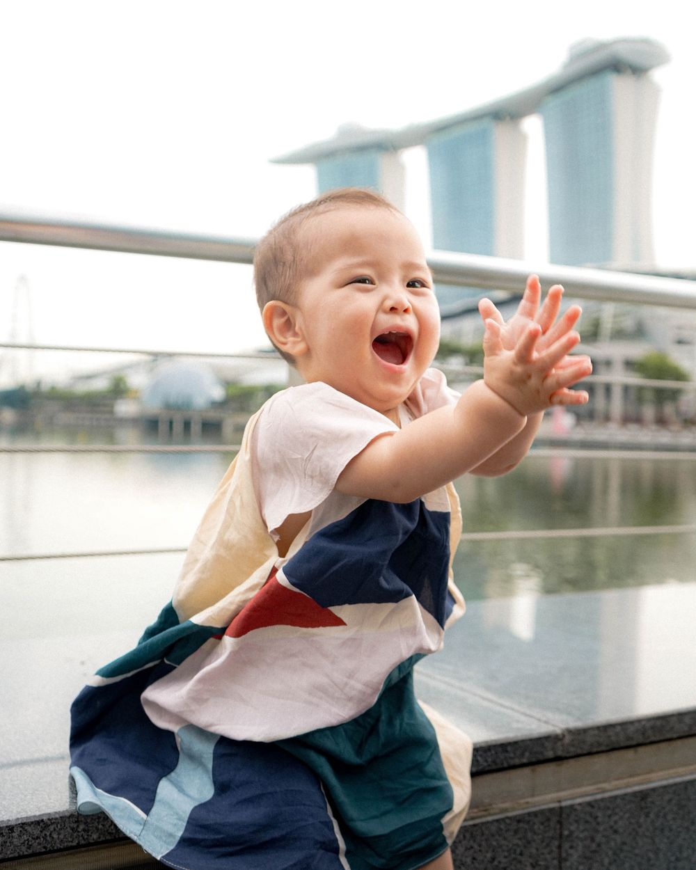 An excited baby claps hands while sitting at Marina Bay waterfront.