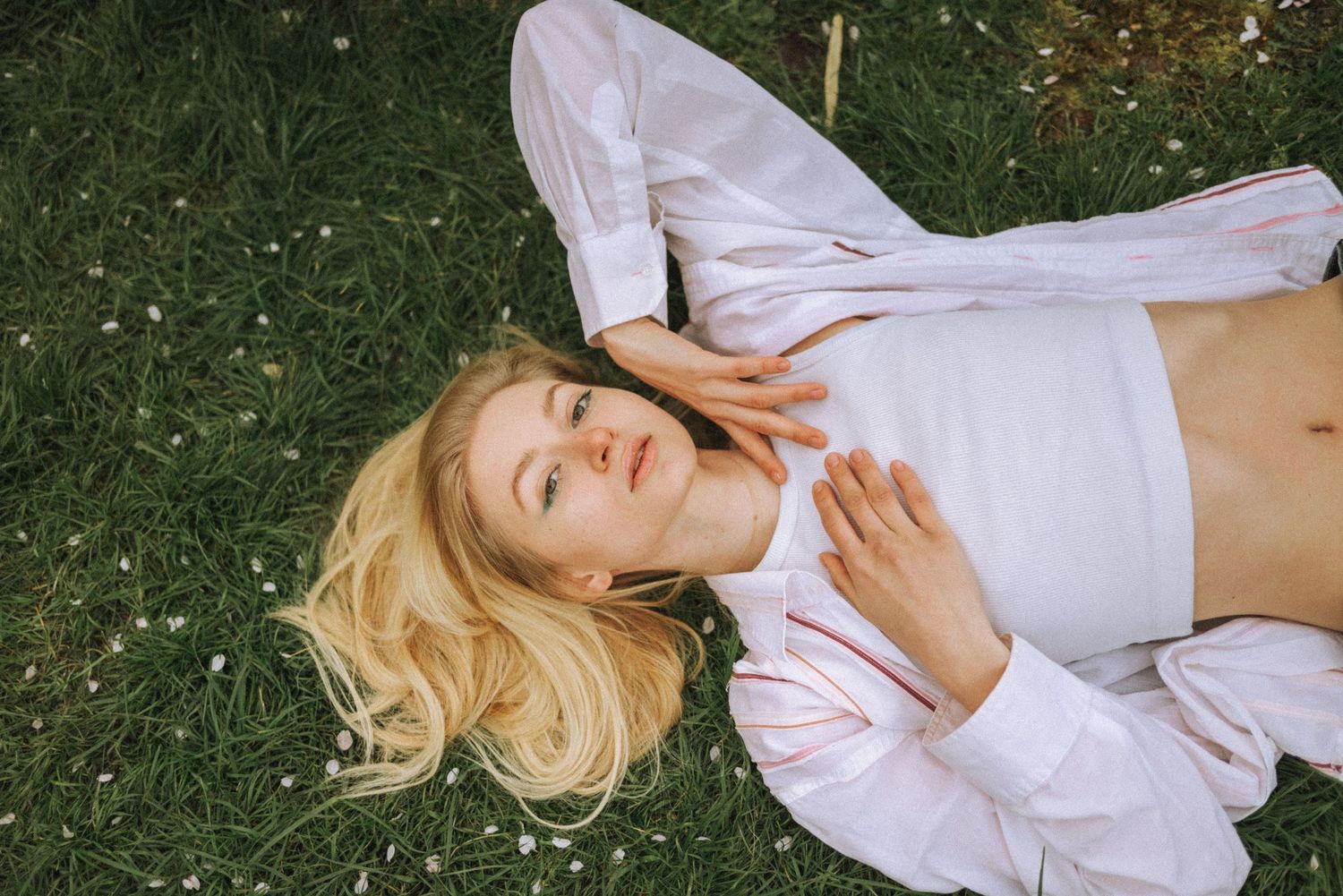 Person lying on grass wearing white clothing in artistic photoshoot sequence.