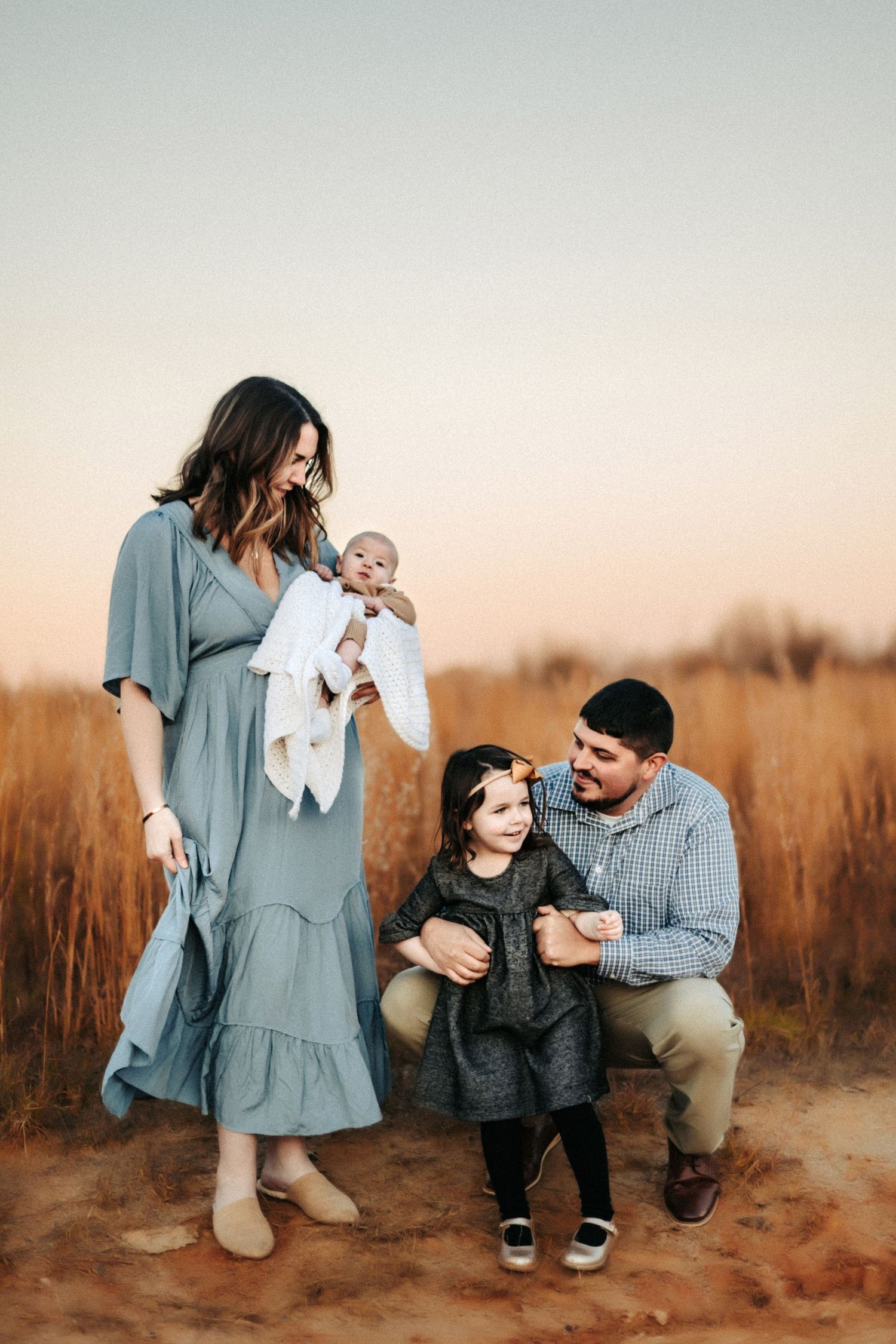 Family of four poses together in a golden field at sunset wearing coordinated blue and grey outfits.