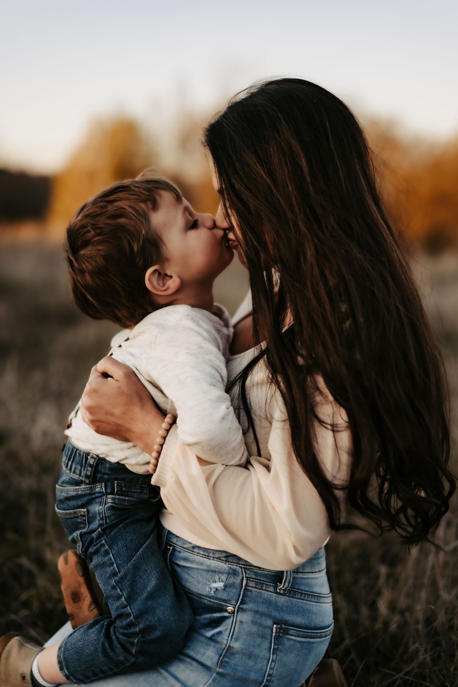 A tender moment between parent and child sharing a kiss at sunset in a rustic field.