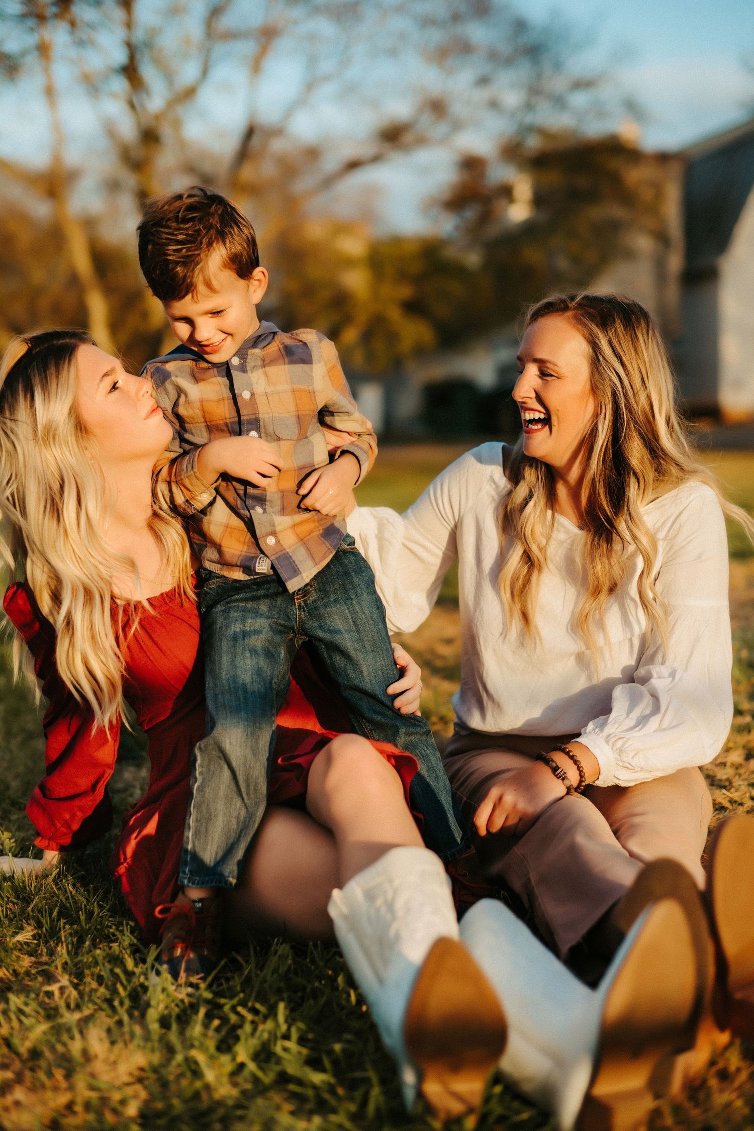 Three people sitting in grass enjoying a warm sunset moment together outdoors in casual fall clothing.
