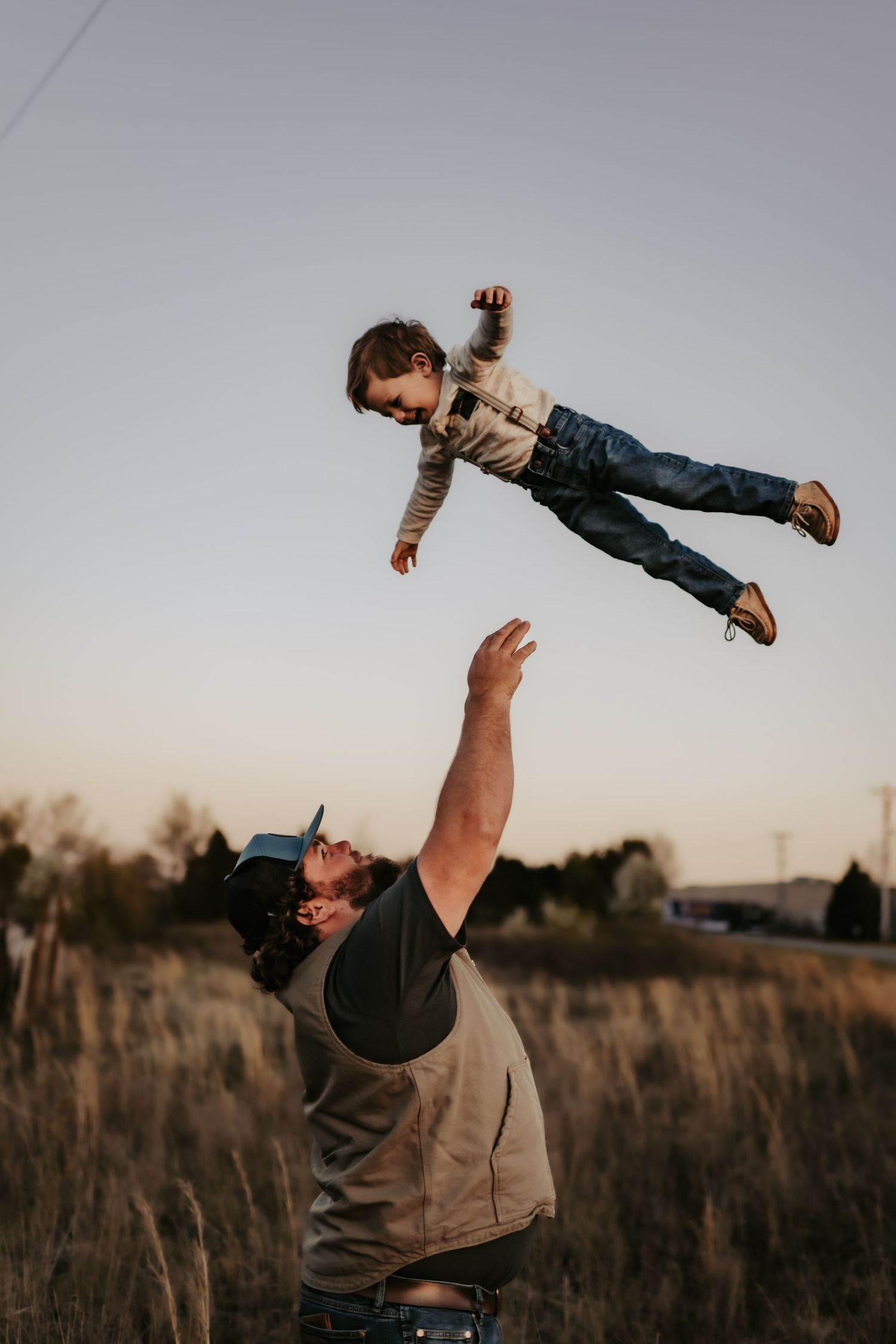 A playful moment captured at sunset as someone tosses a child high into the air in a grassy field.