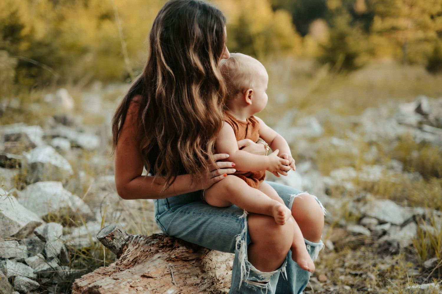 A tender moment between parent and child sitting outdoors on rocks with golden autumn foliage in the background.