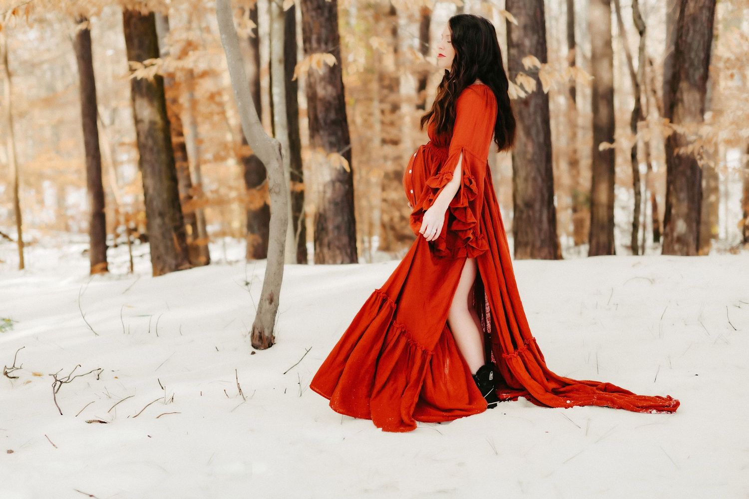 A flowing red dress contrasts dramatically against a snowy winter forest backdrop.