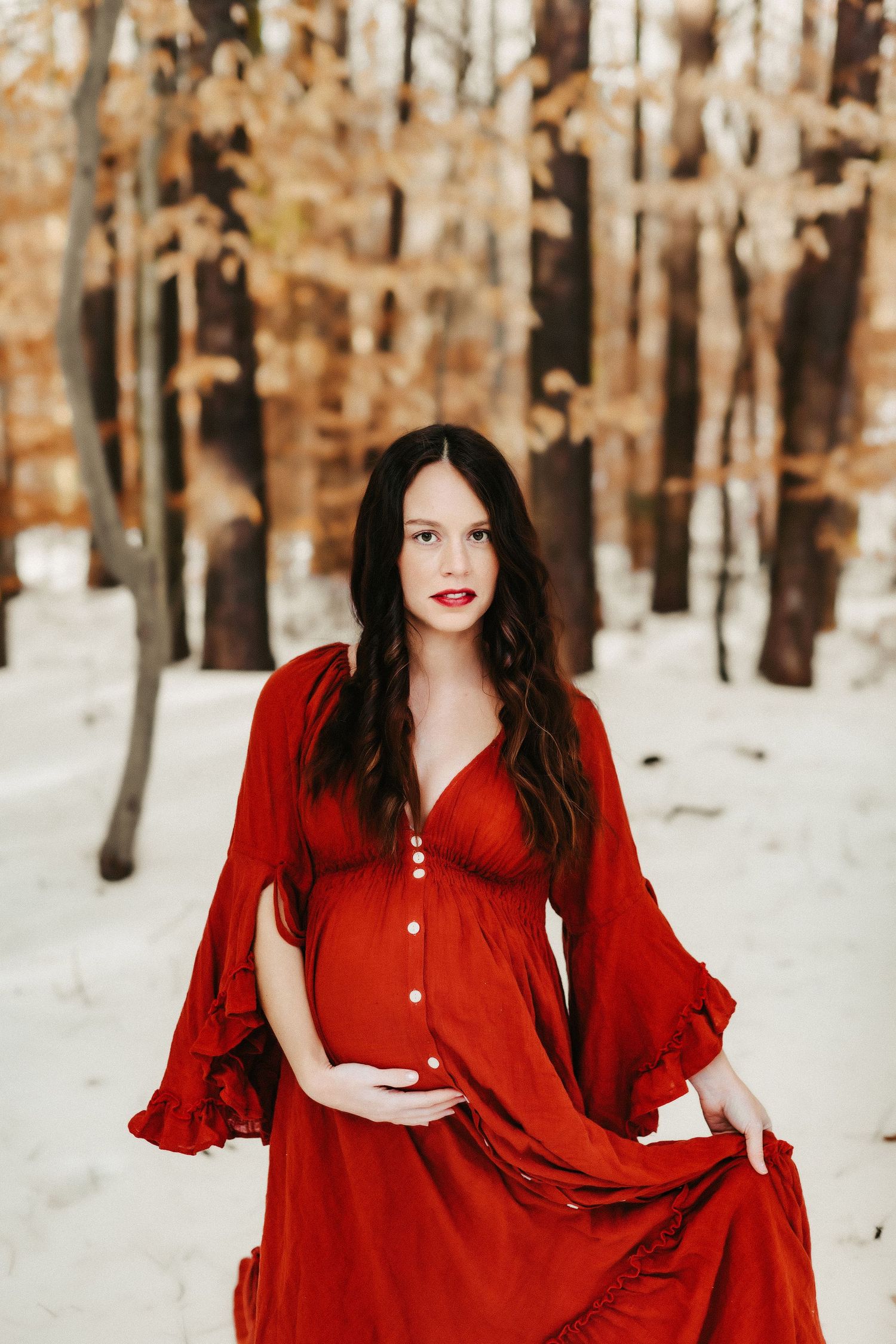 A woman in a flowing red dress stands in a snowy winter forest with white birch trees in the background.