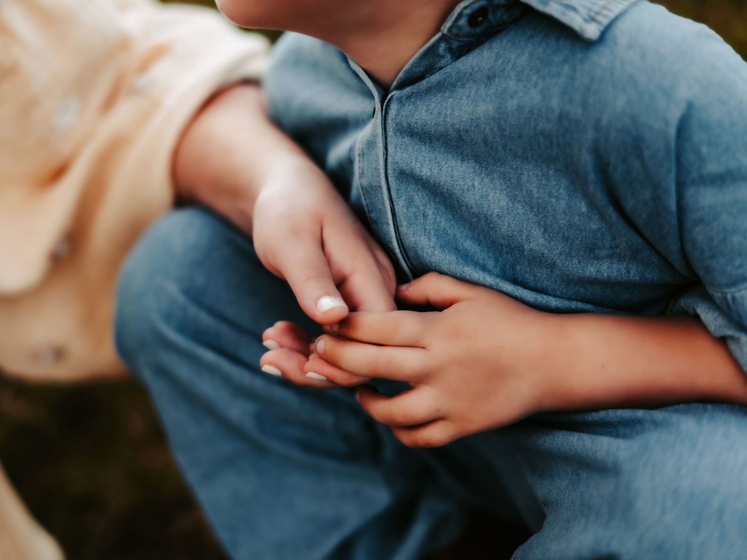 Close up of two hands gently clasped together while wearing a denim shirt.