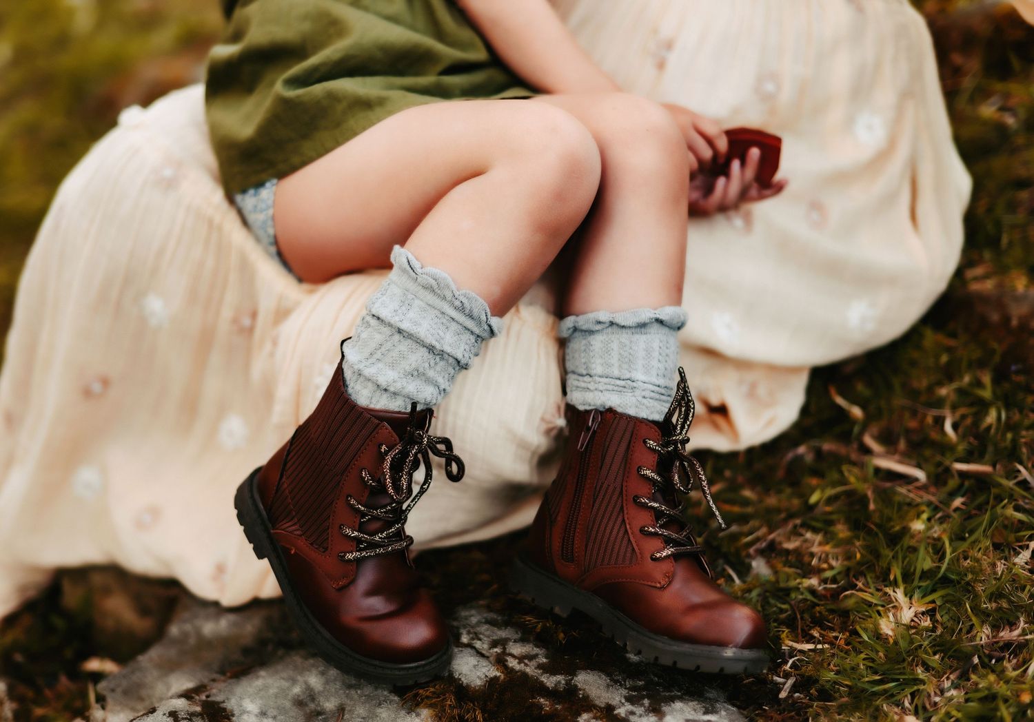 Vintage brown leather boots with folded gray socks on someone sitting in a white dress.