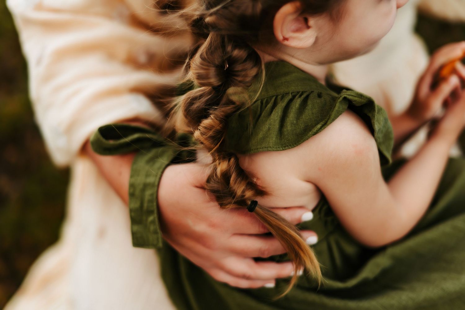 Close-up shot of hands holding a child wearing an olive green sleeveless dress.