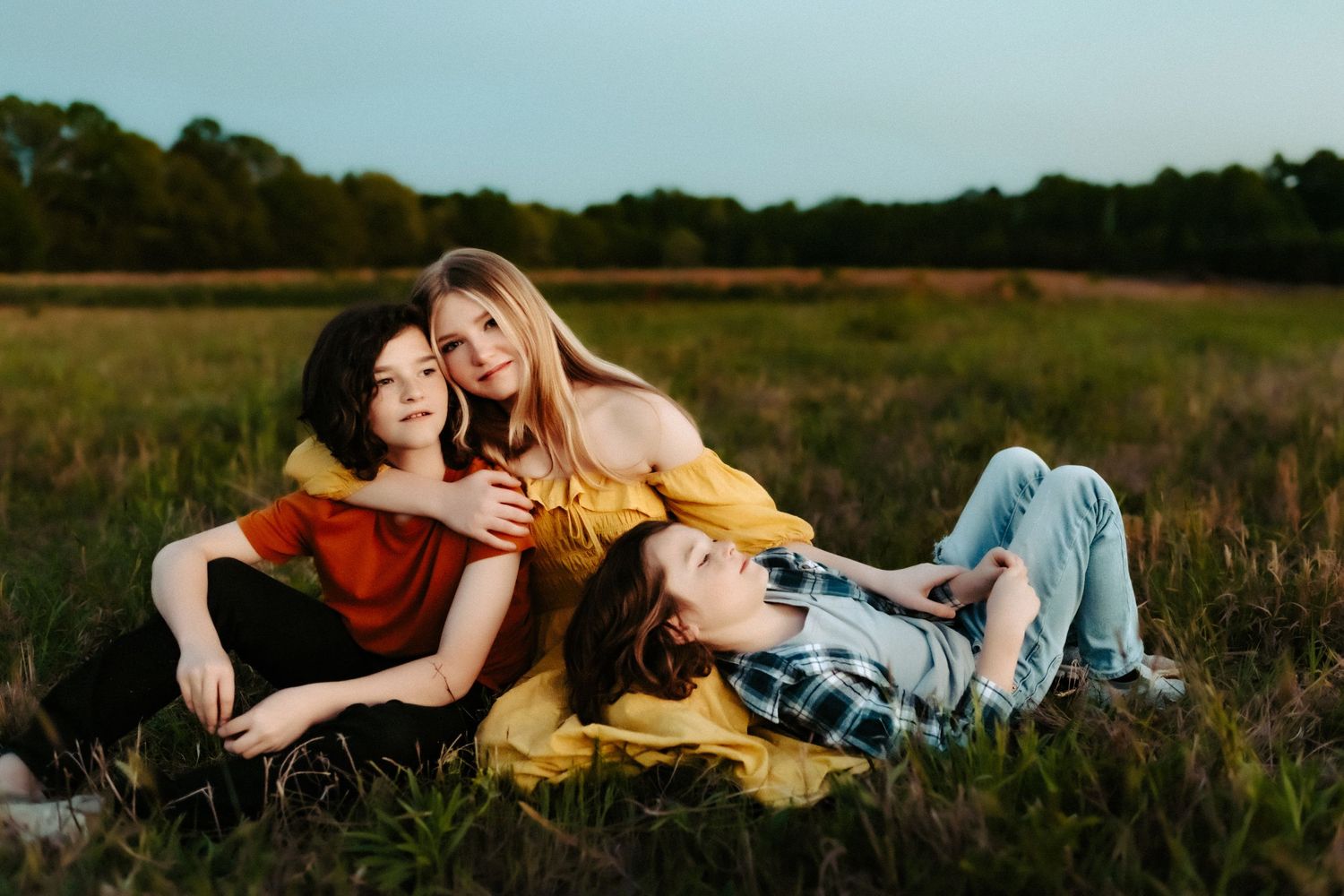 Two people in casual attire lying together and laughing in a grassy field at golden hour.