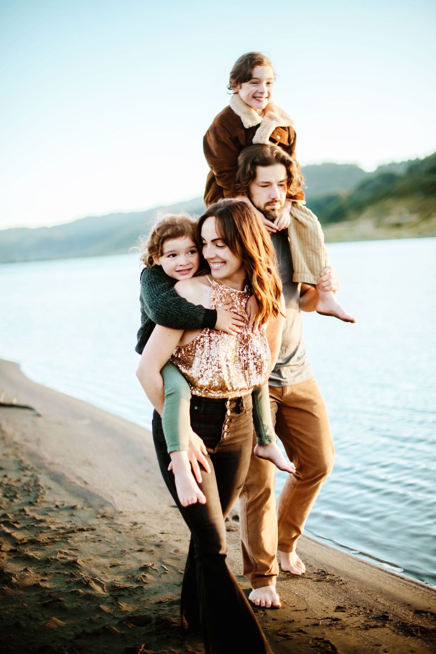 A joyful family embraces while standing along a serene waterfront at sunset.