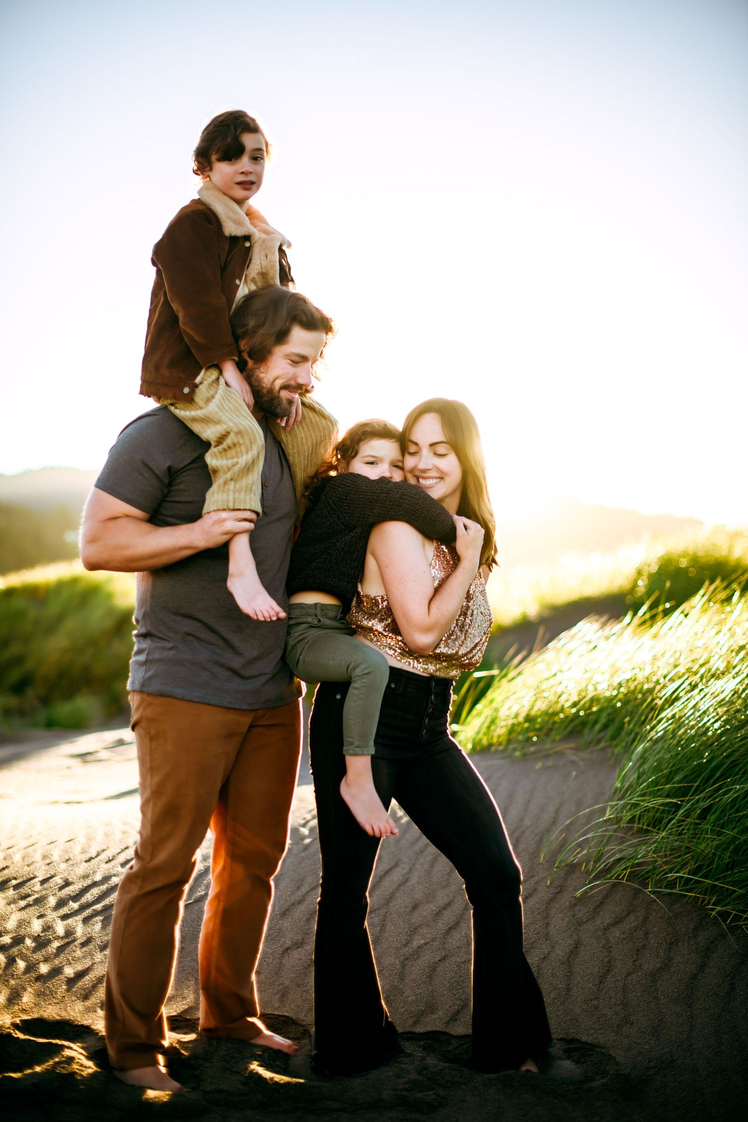 A happy group shares loving embraces while standing together on a grassy hillside at golden hour.