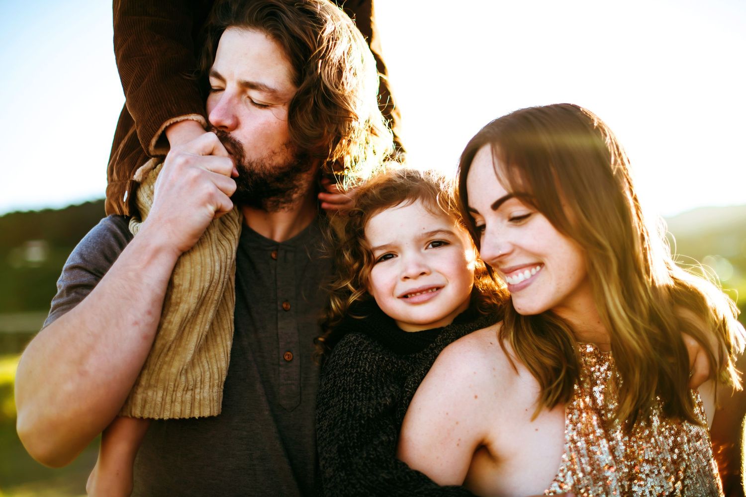 Close family of three sharing a tender warm moment together in golden sunlight outdoors.