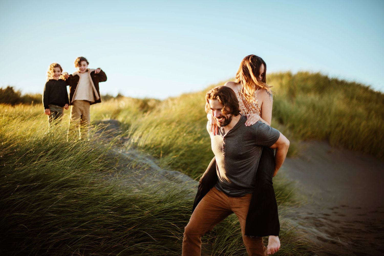 Two couples enjoying a playful sunset moment on grassy dunes near the beach.