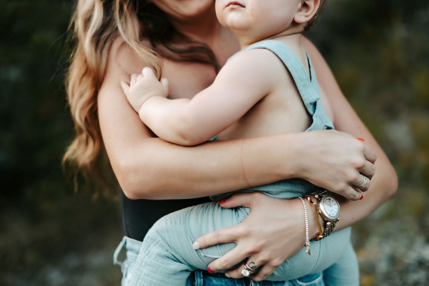 Close up view of loving arms holding a small baby wearing light blue clothing outdoors.