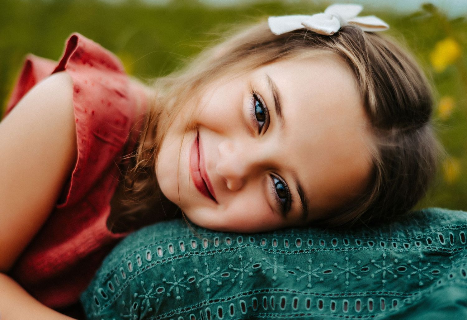 Close-up portrait of someone in a red top resting on a green textured surface with a warm smile.