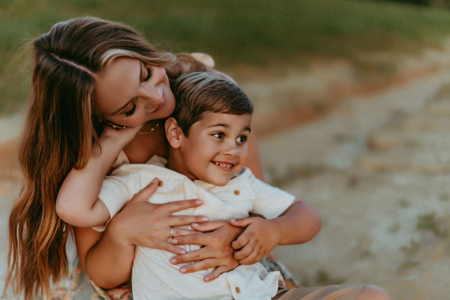 A joyful candid moment of parent and young child embracing outdoors during golden sunset light.