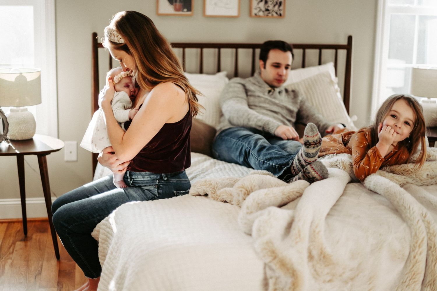 Relaxed family lounging together on white bed during casual morning at home.