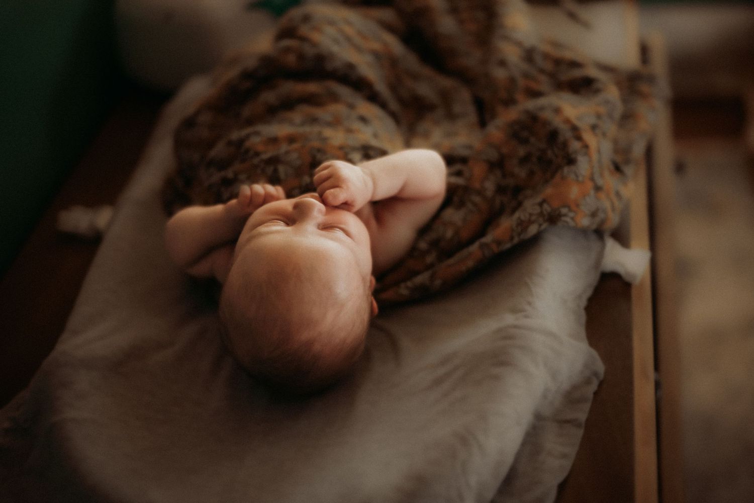 Newborn baby lying on soft blanket in dark moody lighting stretches peacefully during professional photoshoot.