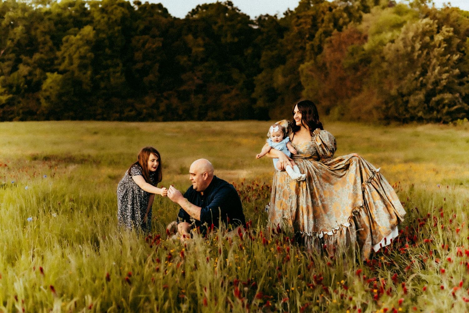 A family enjoys a warm autumn evening together in a golden sunlit meadow surrounded by trees.