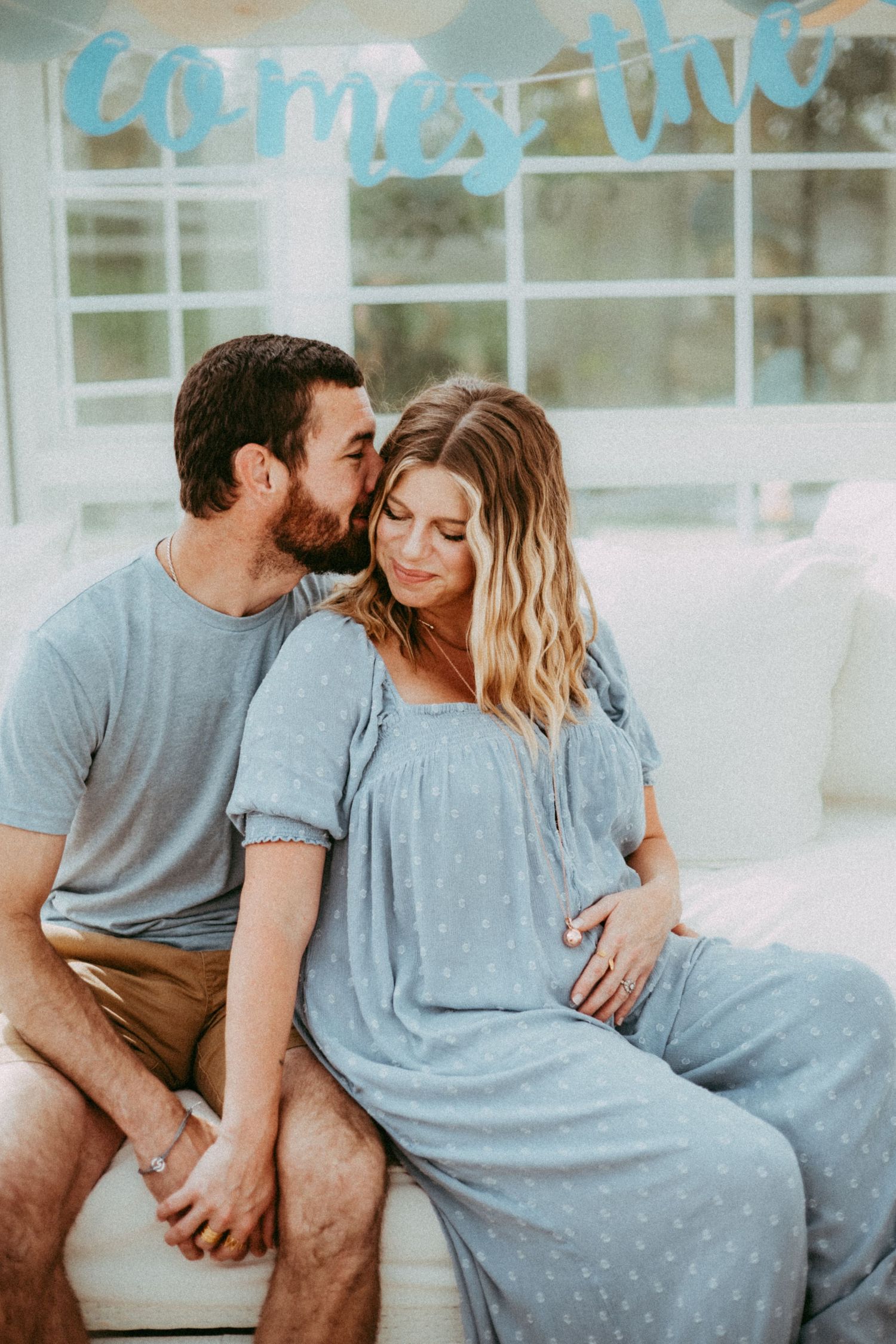 A couple shares an intimate moment together while sitting outside, wearing casual blue and beige clothing.