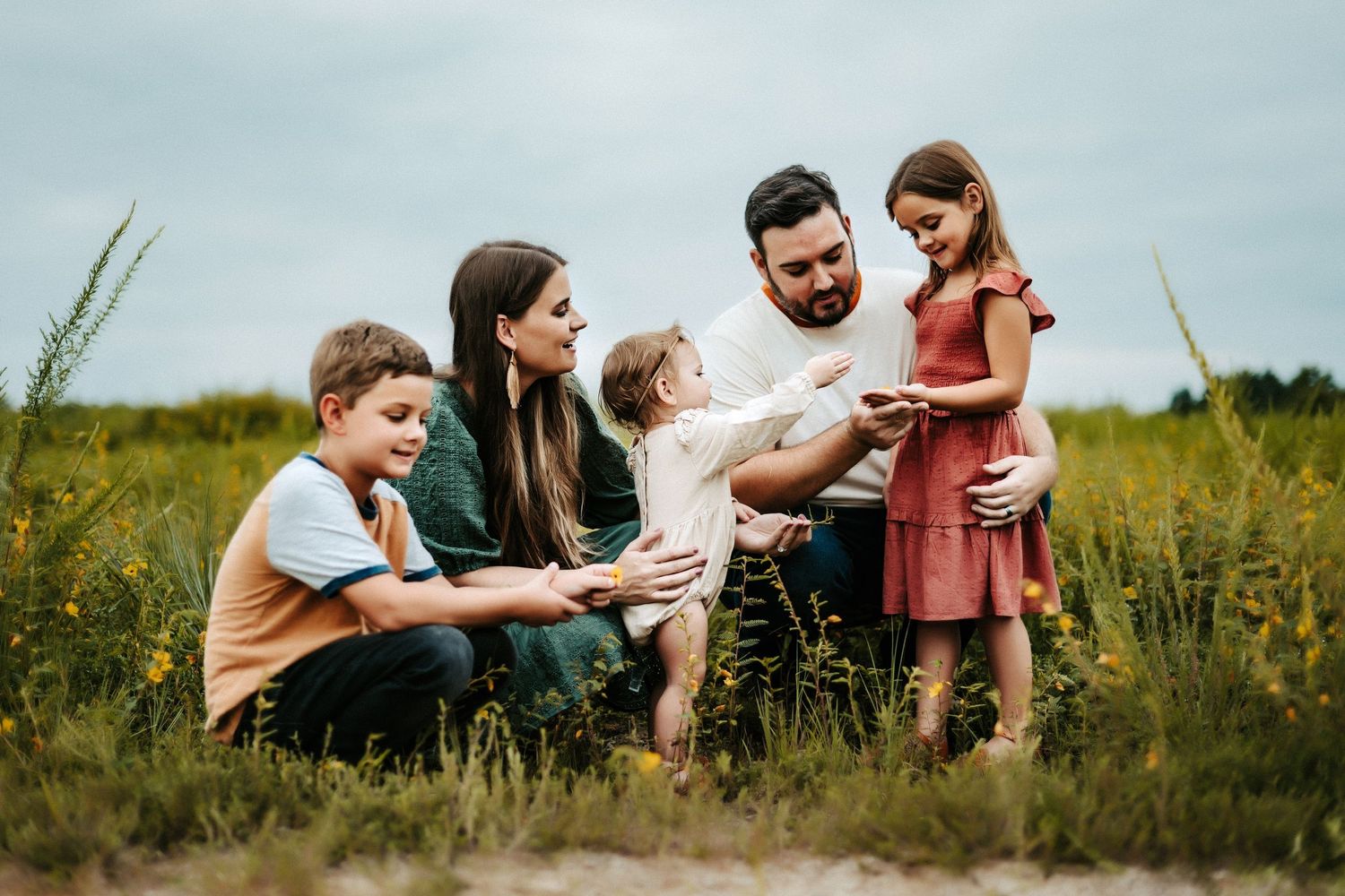 Family of five sitting together in a wildflower meadow while looking at something together on a summer day.