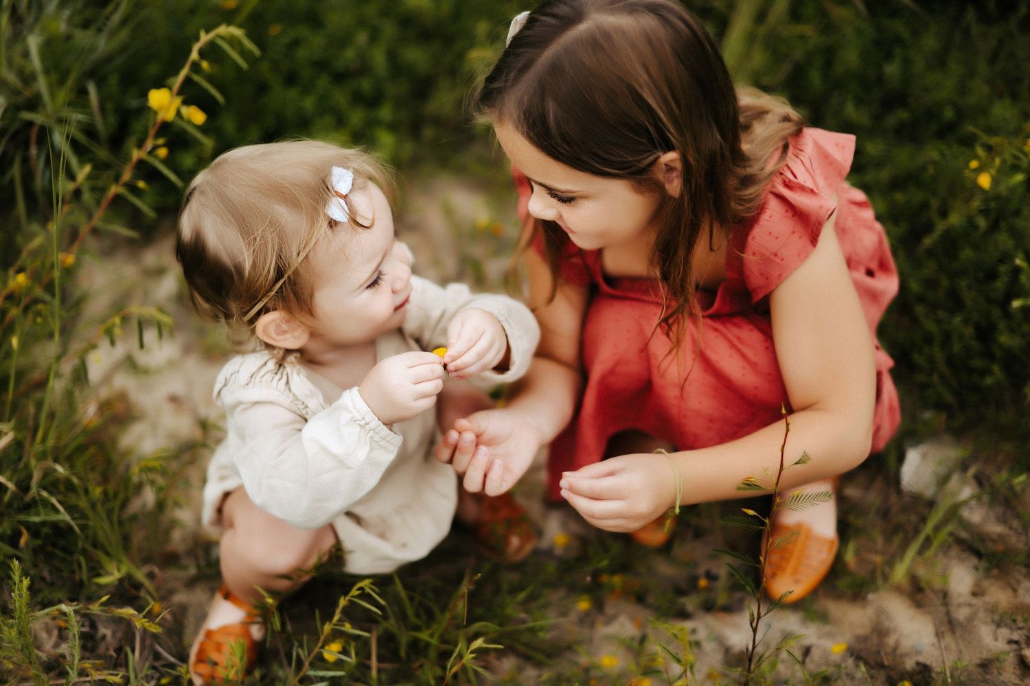 Two people sitting in a garden with yellow wildflowers wearing red and white dresses.