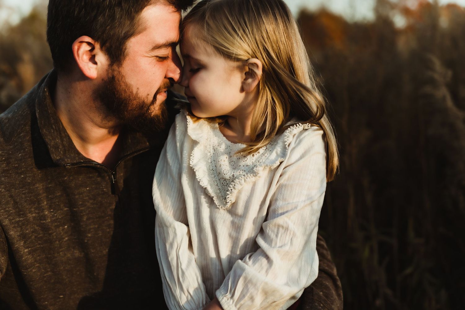 A tender moment between parent and child is captured during golden hour in an outdoor autumn setting.