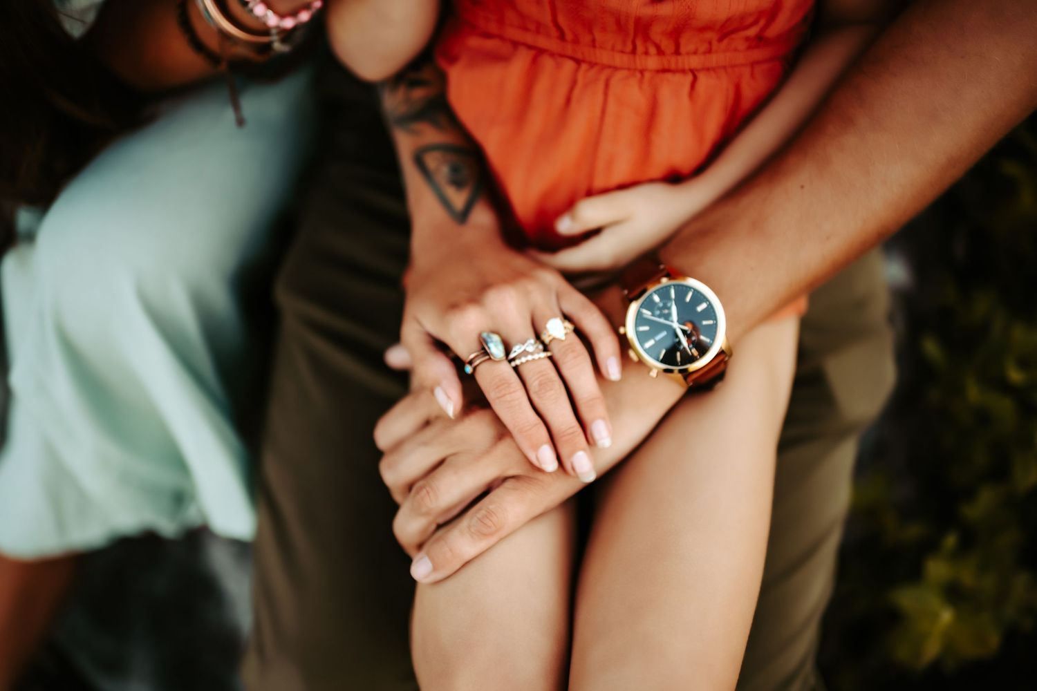 Close-up of hands wearing engagement ring and blue-faced watch during outdoor engagement photoshoot.