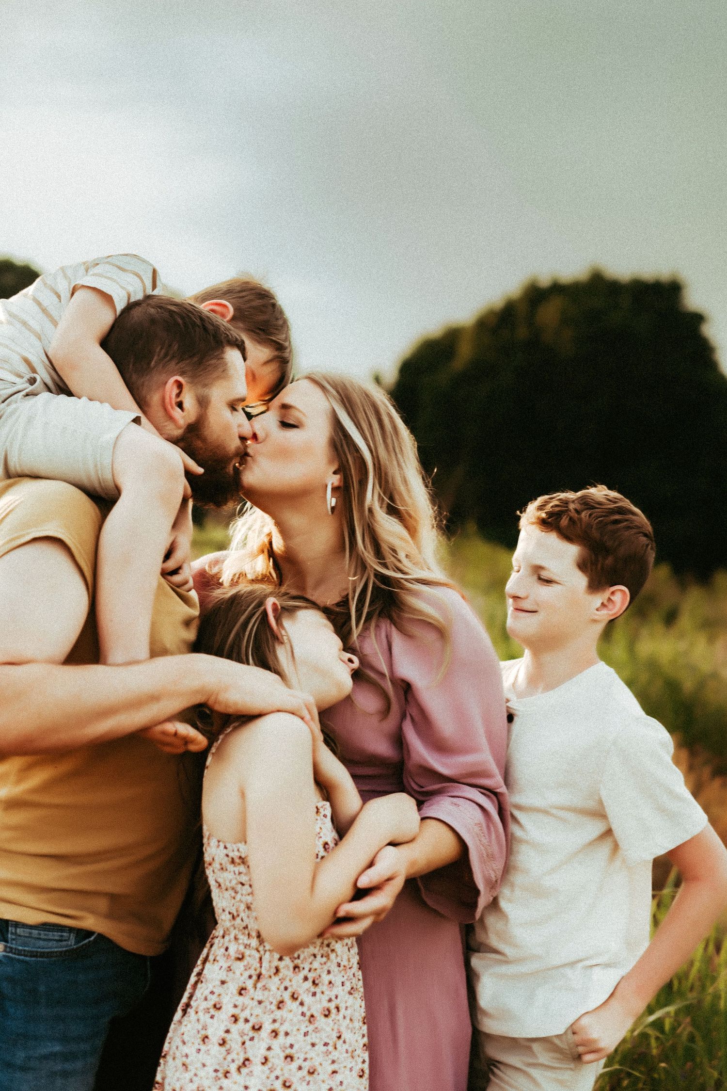 A loving family embraces and shares affectionate moments together during golden hour in a grassy outdoor setting.