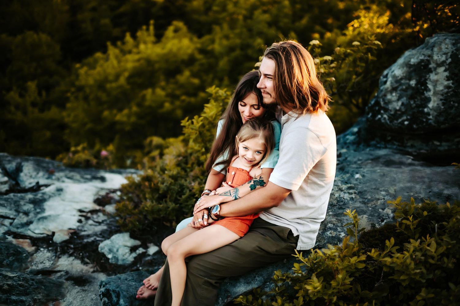 A tender family moment captured on rocky terrain at sunset with golden foliage in the background.