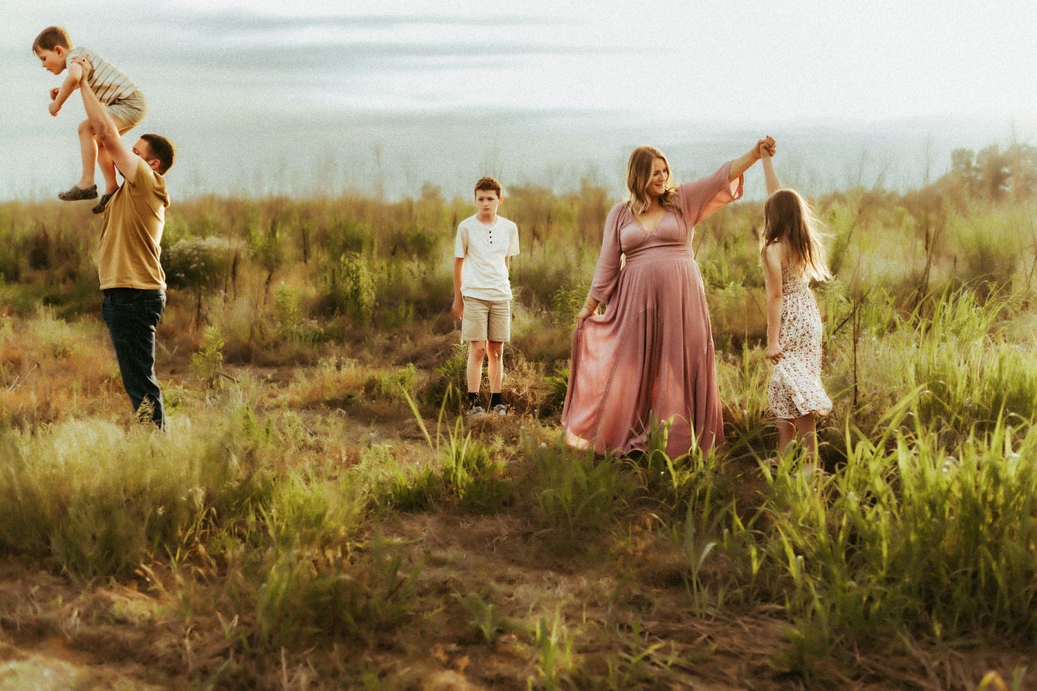 A family enjoys a sunset moment together in a field of tall grass during golden hour.