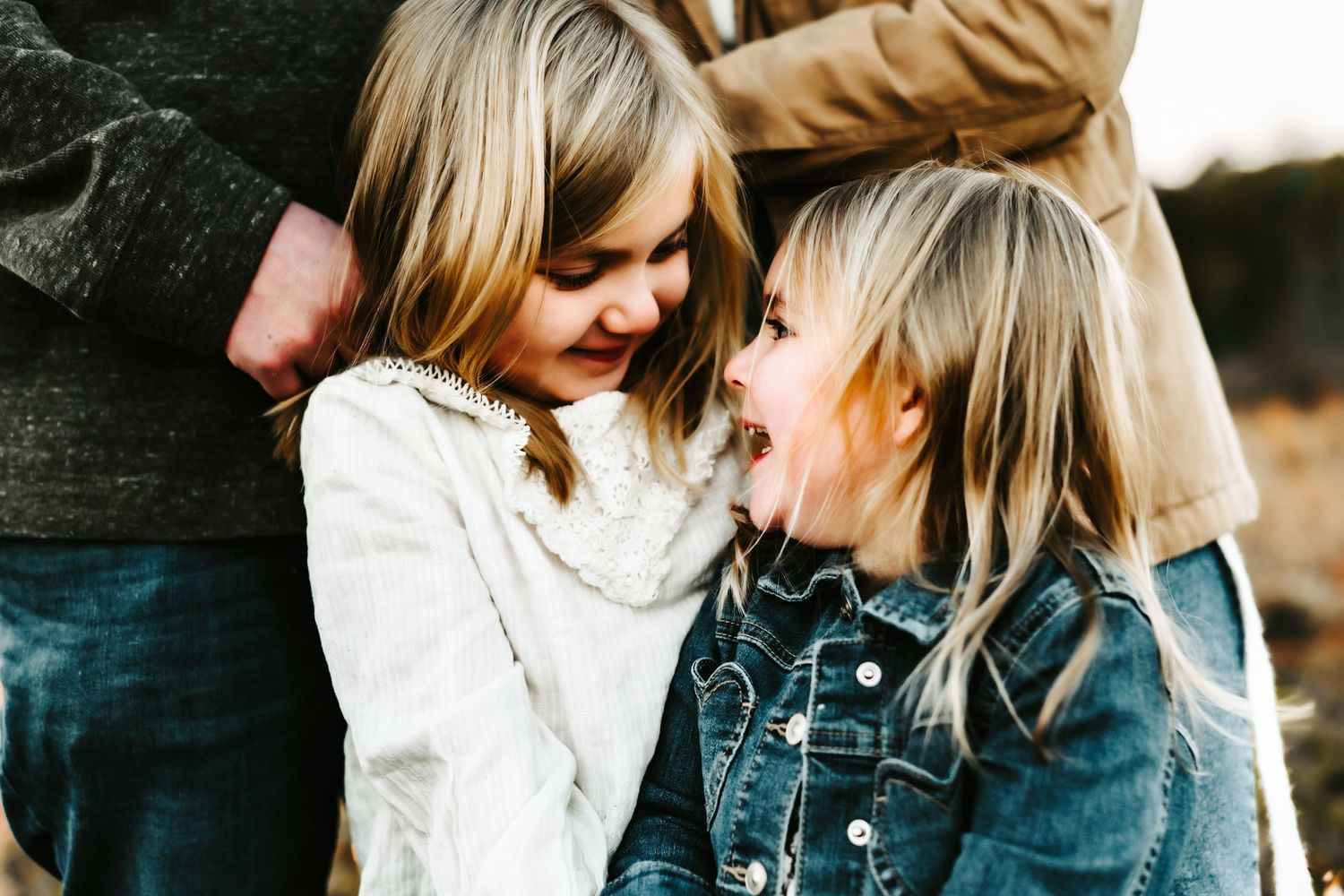 Two children in denim and white tops share a joyful laugh together in an intimate candid moment.