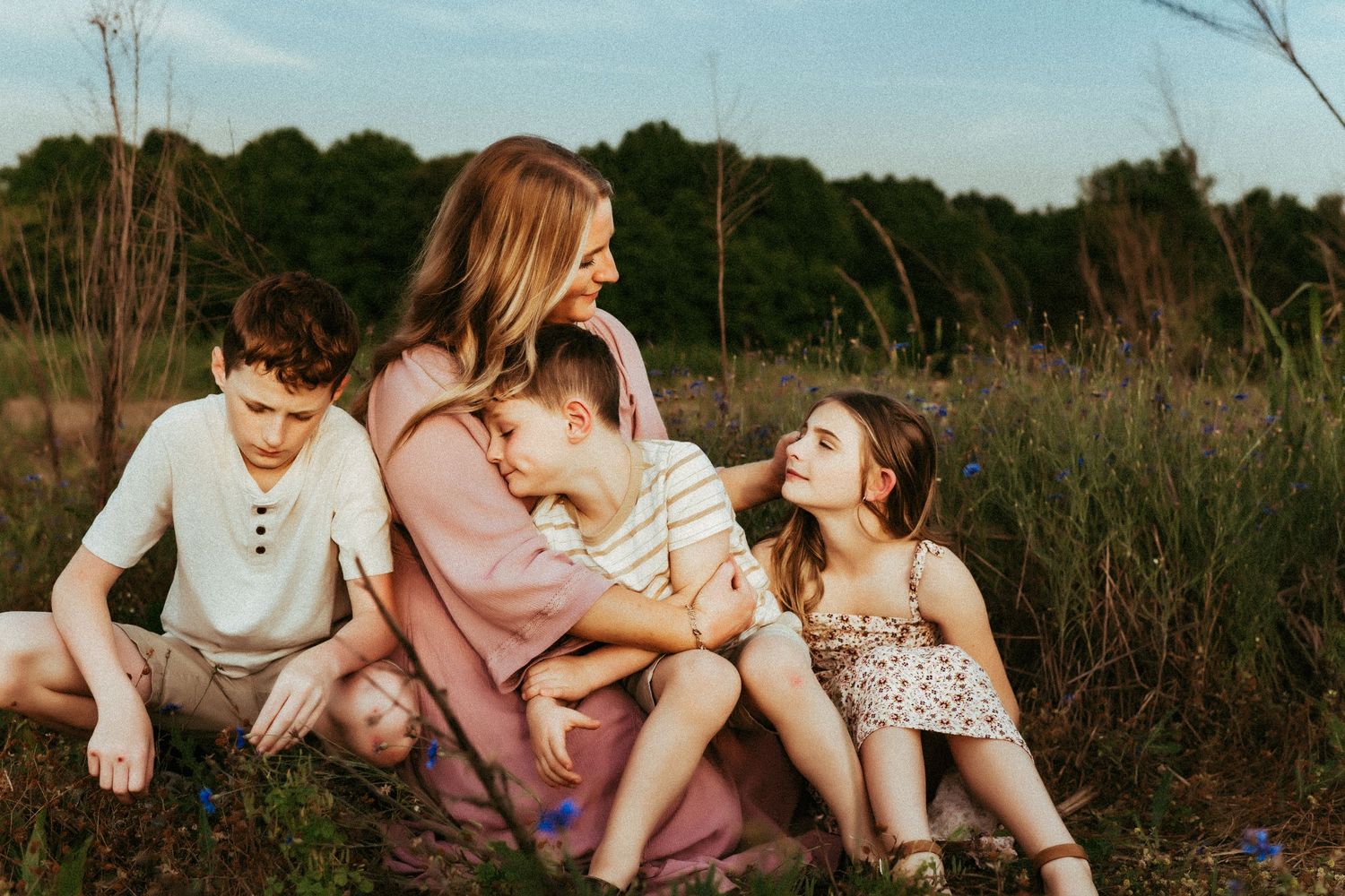 A group sits together on grass surrounded by wildflowers during golden hour in a natural outdoor setting.