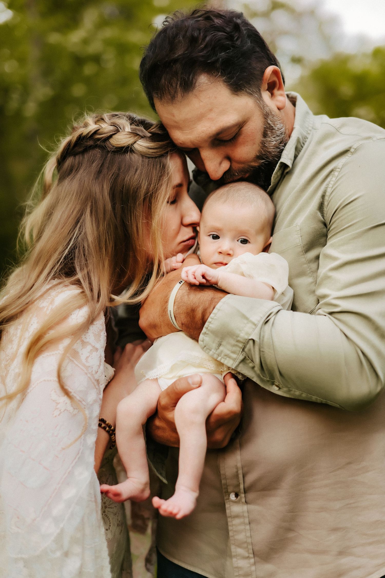 A couple in casual outfits lovingly embraces their small baby outdoors in a tender family moment.