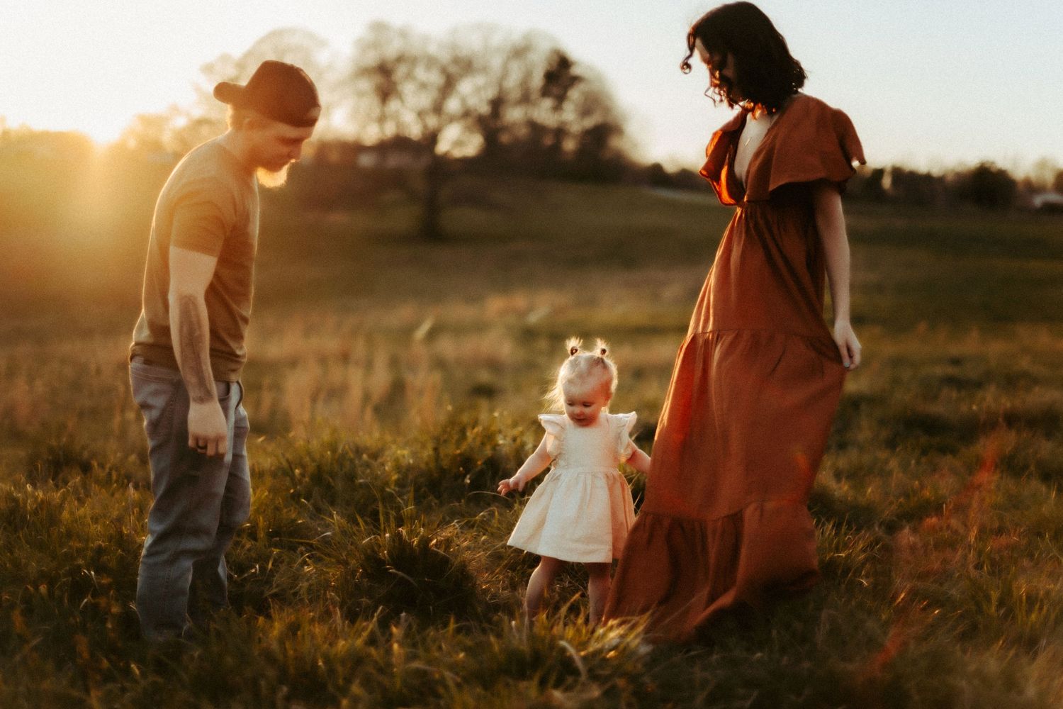 A family enjoys sunset together in a golden field wearing rustic clothing and spinning in warm evening light.