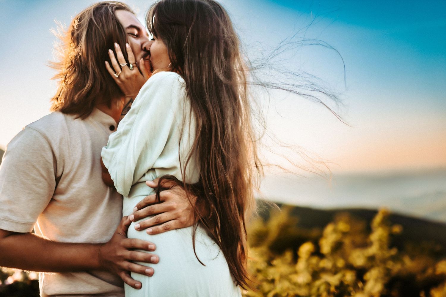 Romantic sunset silhouette of couple embracing against golden sky and mountain backdrop.
