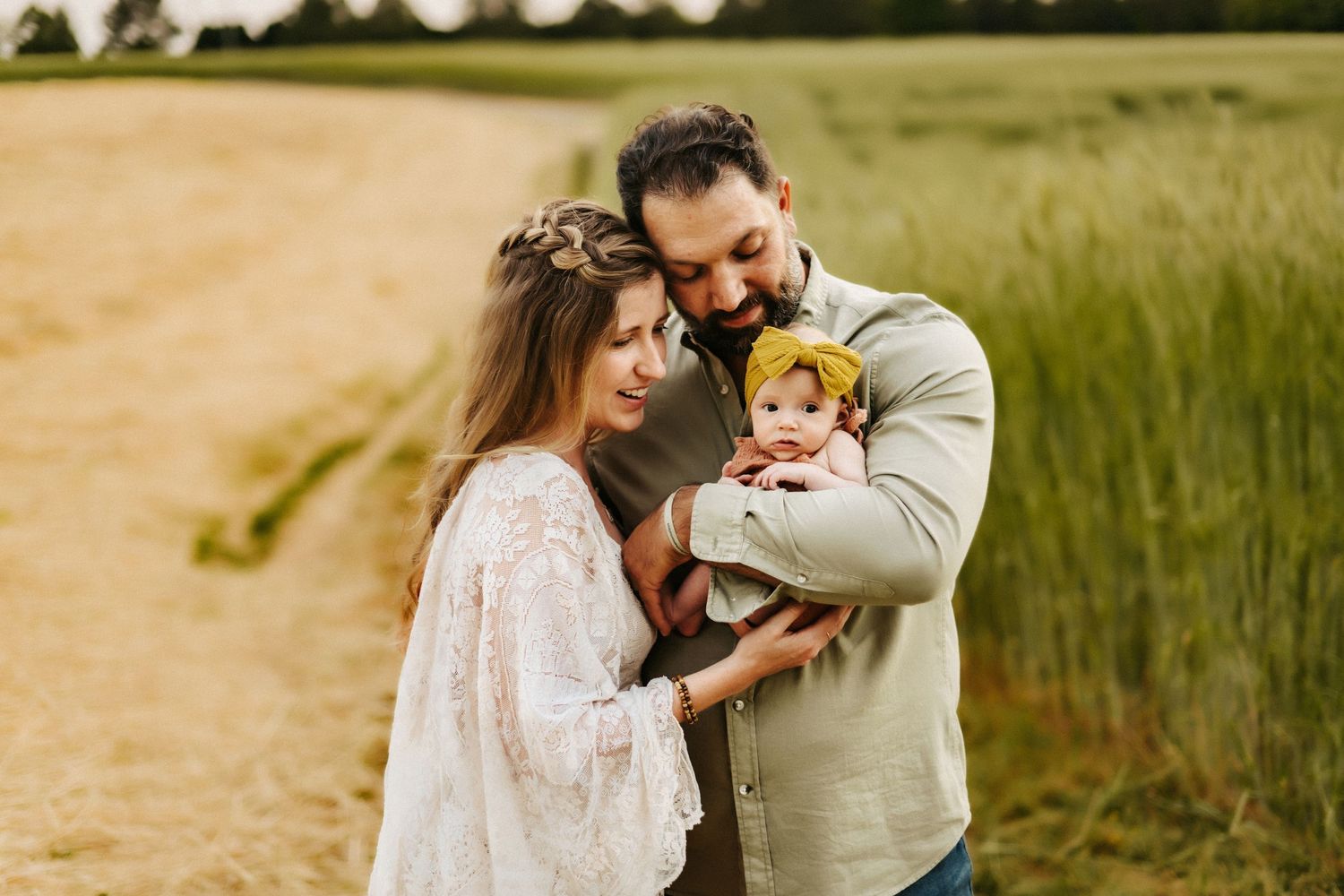 A loving family shares a tender moment together on a dirt path surrounded by tall grass and summer fields.