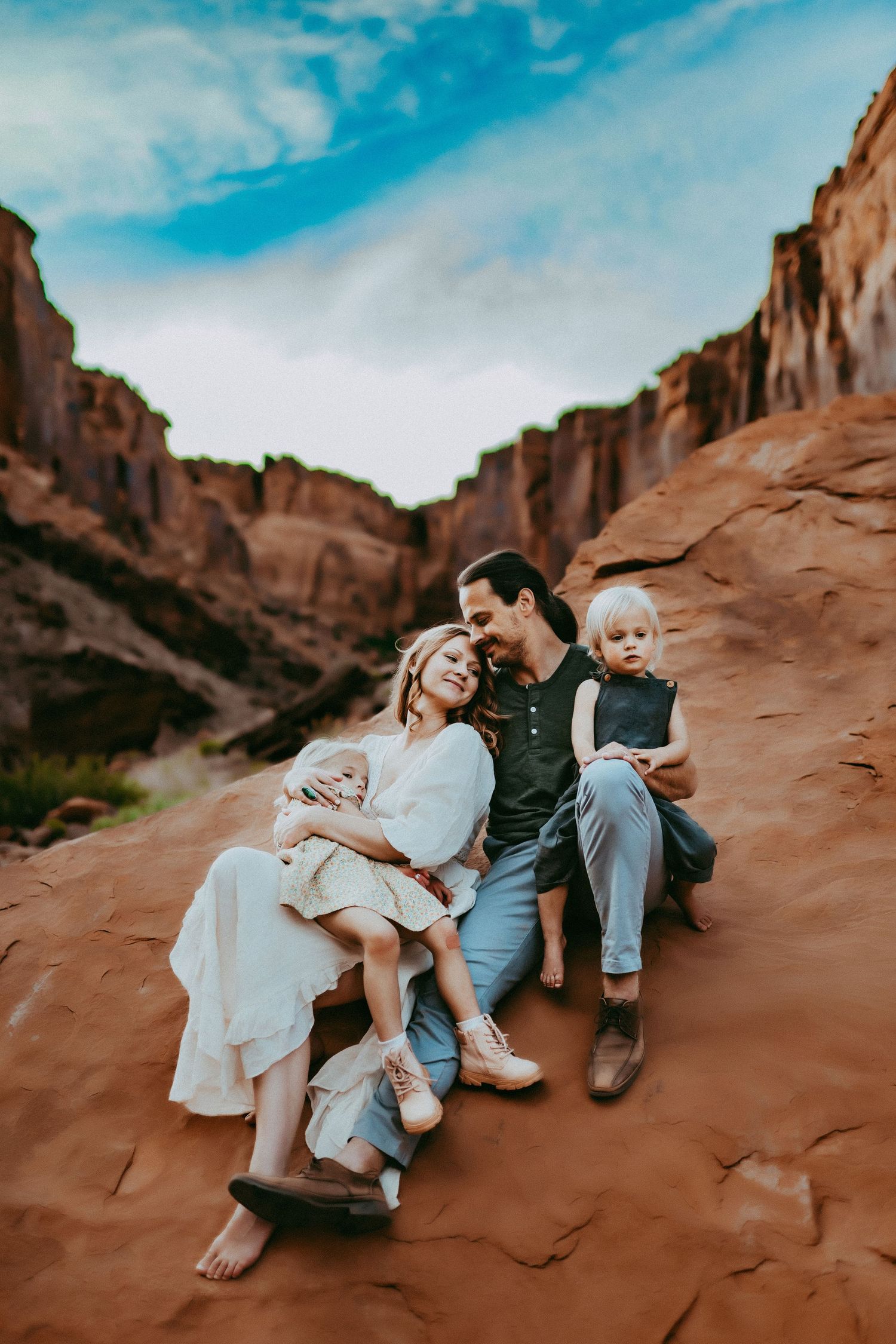 A group sits together on red rock formations at sunset in Moab against towering sandstone cliffs and blue sky.