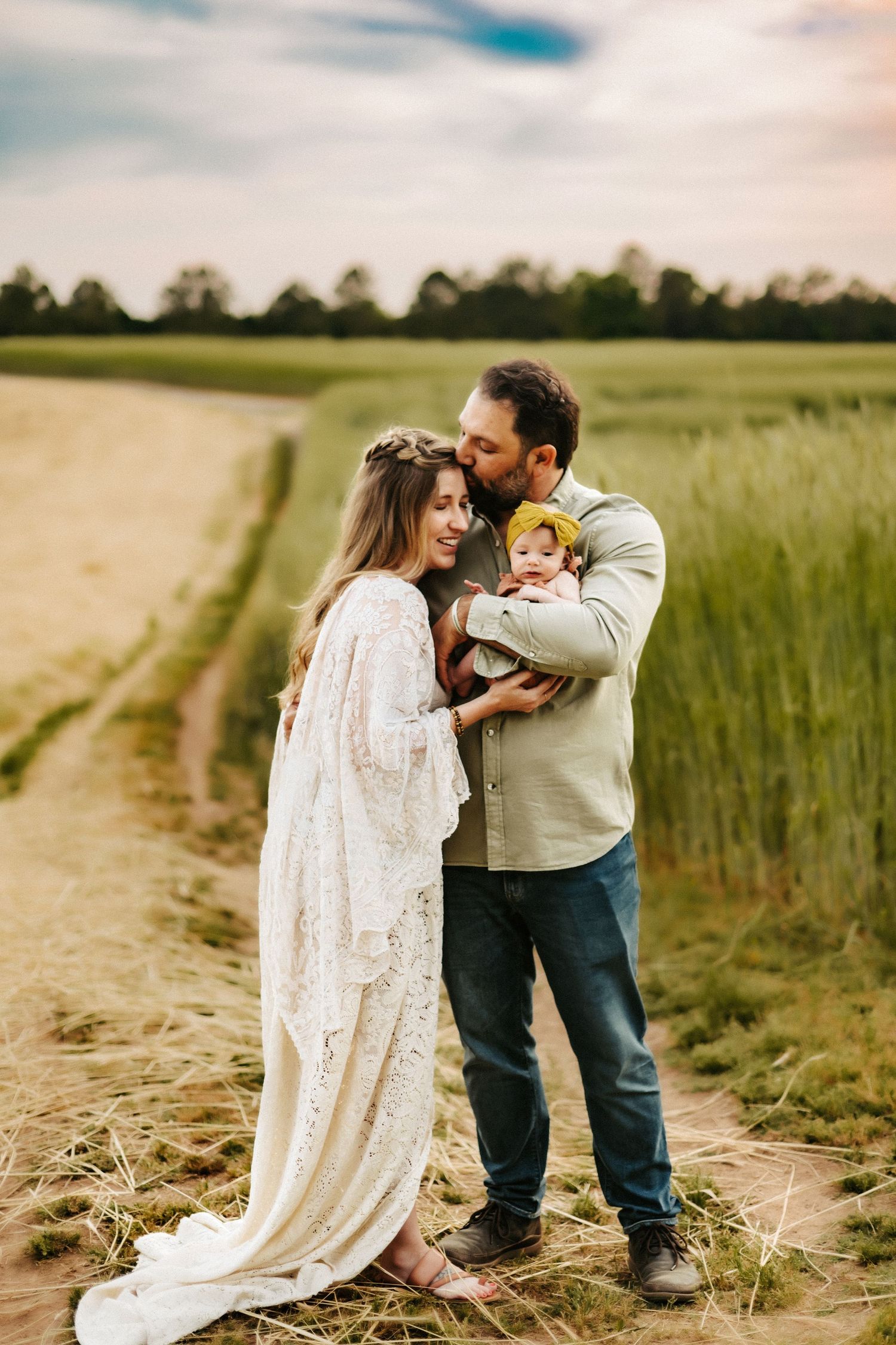 A family shares an intimate moment together on a dirt path surrounded by green fields during golden hour.