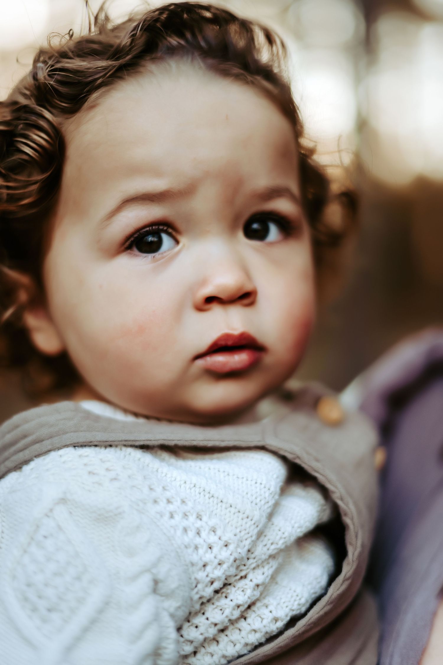 Close up portrait of a young child with large brown eyes and curly hair wearing a light knit sweater.