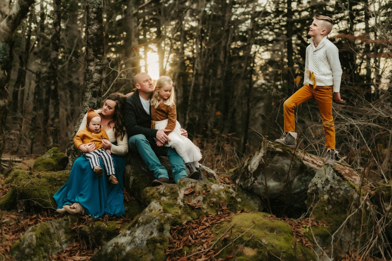 Group sitting on mossy rocks in a sunlit forest at sunset wearing coordinated blue and orange outfits.