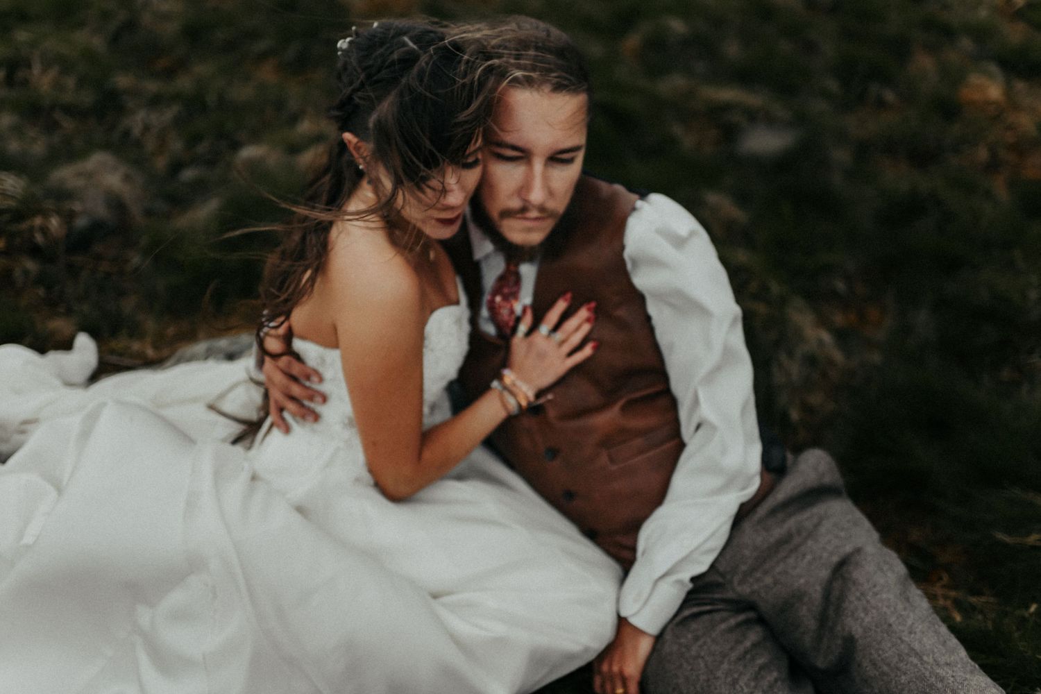 A couple share an intimate moment outdoors on their wedding day, the bride in white and groom in a brown vest.