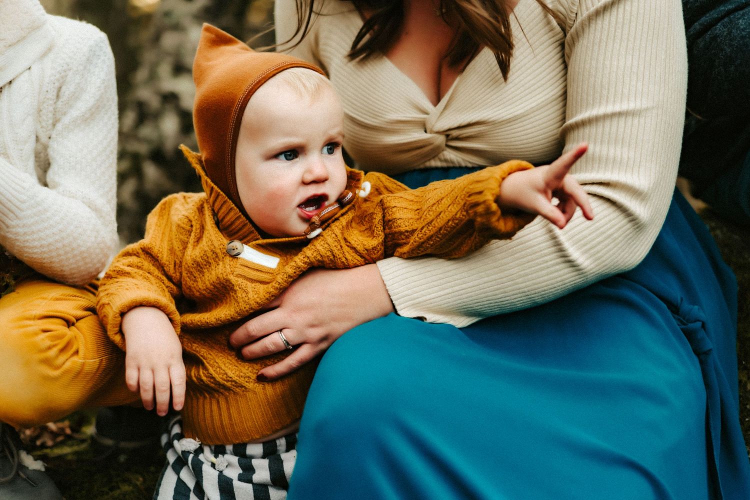 Baby wearing cozy mustard yellow sweater sits in lap wearing cute animal ears outfit.